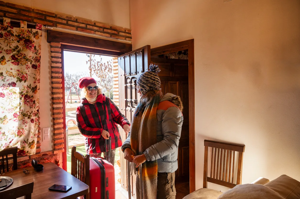 Two people in winter clothing carrying their suitcases into a holiday let